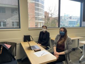 Megan Butchart and Sarah Cipes sit at a desk wearing face masks and sitting in front of a laptop.