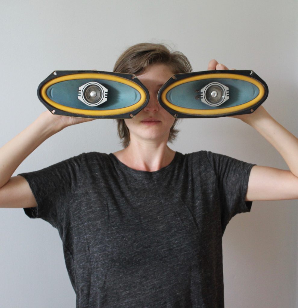 A white woman wearing a black tshirt holds up two large oval shapes over her eyes.